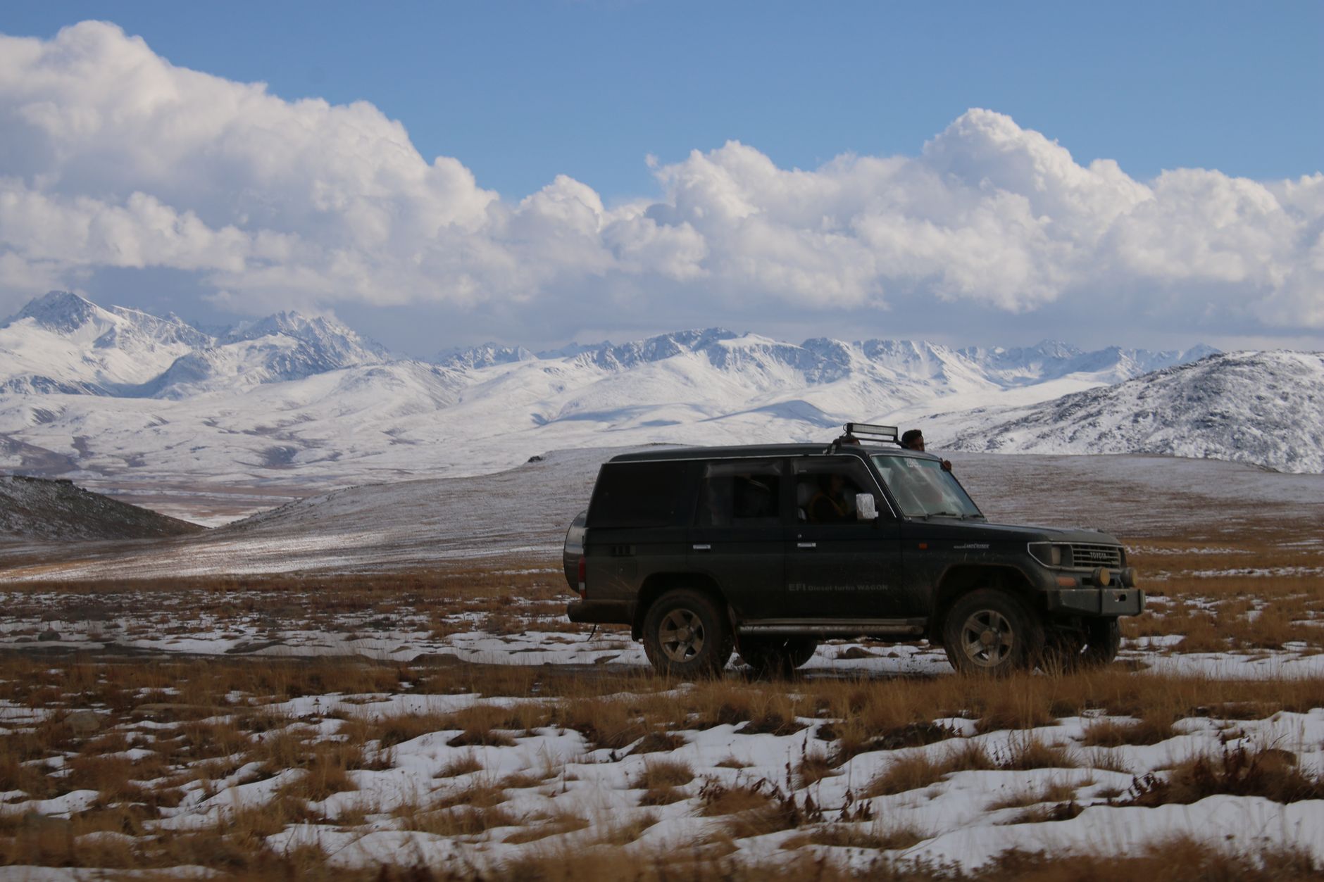 A white 4x4 turbo-diesel car parked in the high-mountain, green landscape of the Egrisi Range, with Caucasus peaks visible in the background.