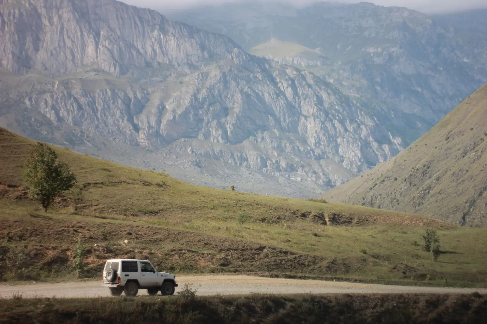 White SUV on a mountain road with a view of Kazbegi in Georgia