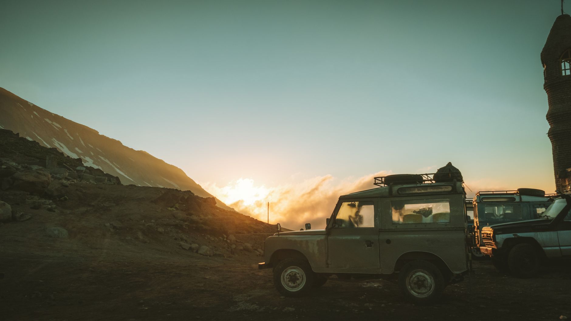 A white 4x4 off-road vehicle parked against the backdrop of the Caucasus Mountains on a challenging Georgian mountain road.