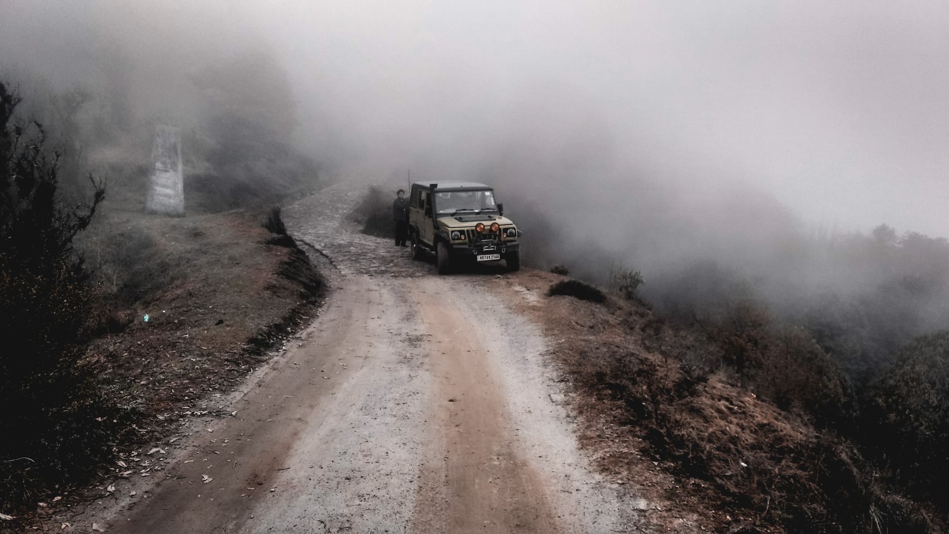 A white 4x4 jeep driving along a narrow, rocky mountain road in Kazbegi on a sunny day